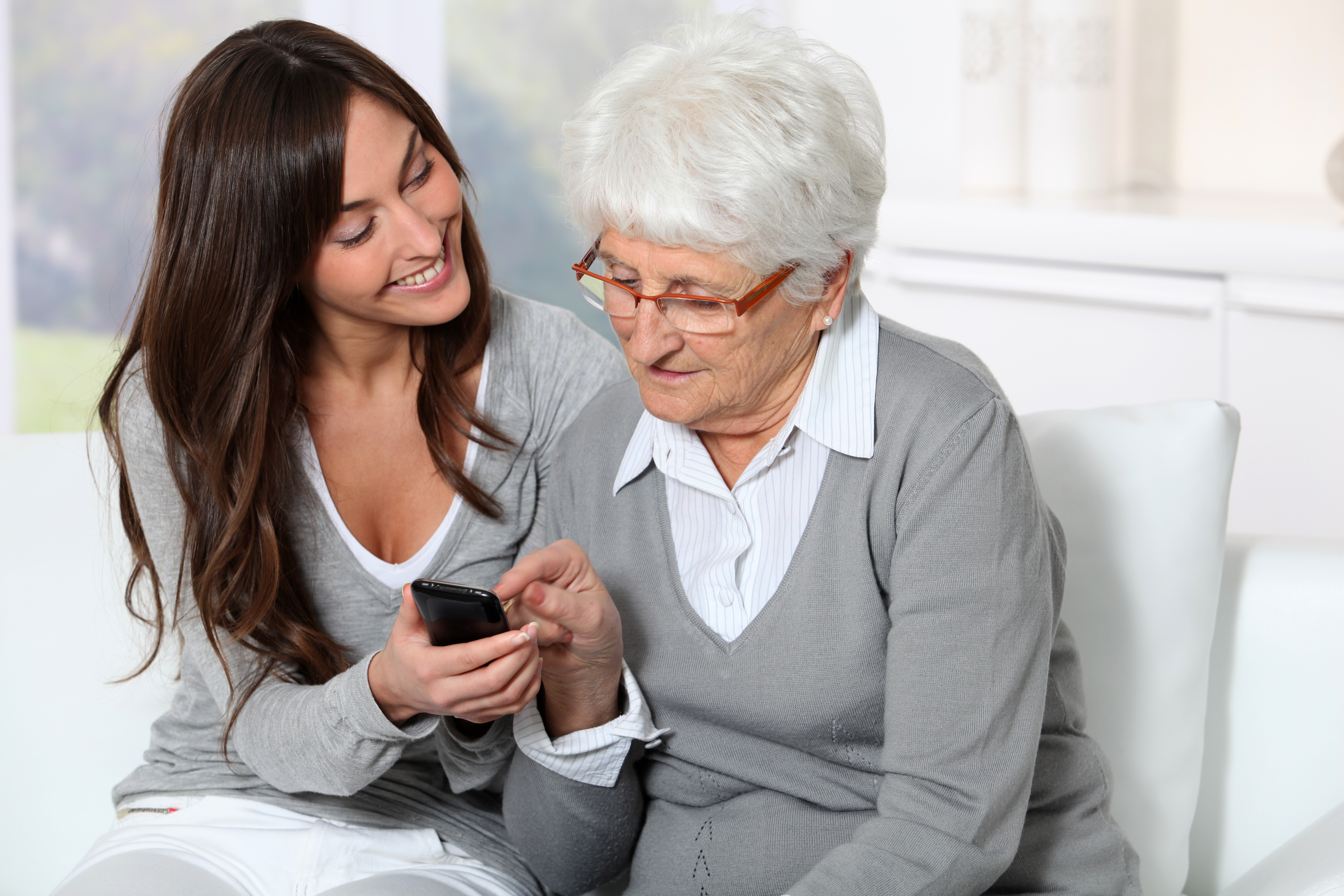 Young woman showing how to use mobile phone to grandmother